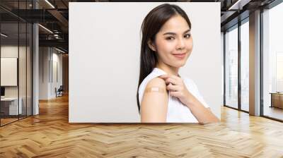 Vaccination. Young beautiful asian woman getting a vaccine protection the coronavirus. Smiling happy female showing arm with bandage after receiving vaccination. On isolated white background. Wall mural