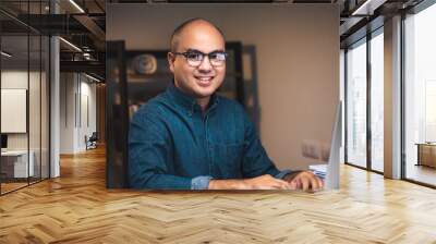 Young asian businessman working with computer in the dark office at night. Attractive handsome Indian man work hard overtime in home with floor lamp ambient warm light late at night Wall mural