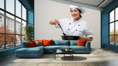 Young beautiful asian woman chef in uniform holding turner and iron Frying pan utensils cooking in the kitchen various gesture on isolated background. woman occupation chef restaurant and hotel. Wall mural