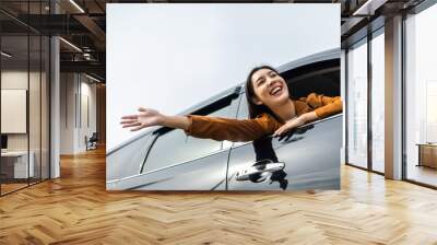 Young beautiful asian women getting new car. she very happy and excited. Smiling female driving vehicle on the road on a bright day. Sticking her head outta the windshield Wall mural