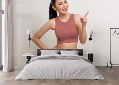 Young beautiful smiling asian woman with sportswear pointing finger to copy space on isolated. Happy healthy slim fit and firm latin attractive sporty woman standing pose exercise workout in studio. Wall mural