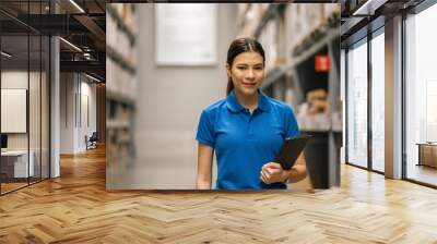 Young female worker in blue uniform checklist manage parcel box product in warehouse. Asian woman employee holding tablet working at store industry. Logistic import export concept. Wall mural