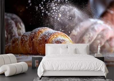 A baker's hands dusting a freshly baked croissant with flour on a wooden counter, capturing the art of baking. Wall mural