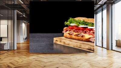 Submarine sandwich with ham, cheese, lettuce, tomatoes,onion, mortadella and sausage on black background. Copy space Wall mural