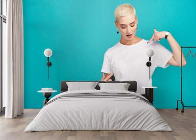 Just waiting for your words.... Studio shot of a confident young woman pointing at her t shirt against a turquoise background. Wall mural