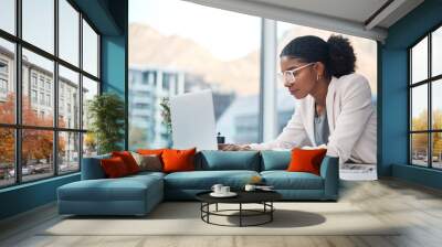 Data professional and secretary typing an email on a laptop and doing online research while working in an office. African entrepreneur looking focused while using the internet for work Wall mural