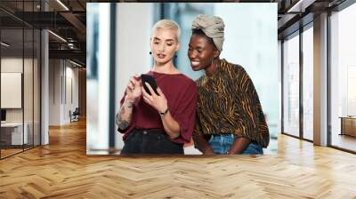 Let me show you some of my images. Cropped shot of two attractive young business colleagues sitting in the office together and using a cellphone. Wall mural