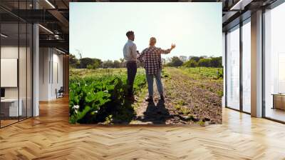 Live life to the greenest. Rearview shot of two young farmers looking at a tablet while working on their farm. Wall mural