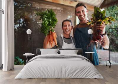 Pick your favorite. Portrait of a happy young couple posing together holding bunches of freshly picked carrots and beetroot at their farm. Wall mural