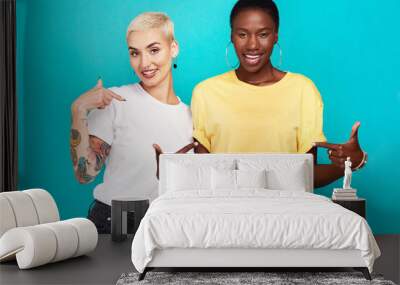 Speak your truth. Studio shot of two confident young women pointing at their t shirts against a turquoise background. Wall mural