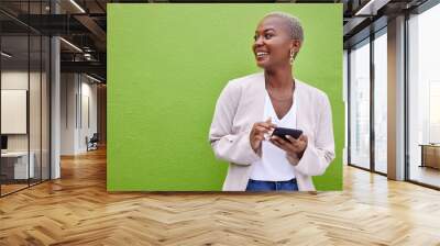 Woman, thinking and phone for communication by a wall or green background with internet. Happy African female person outdoor with a smartphone for social media, networking app and chat mockup space Wall mural