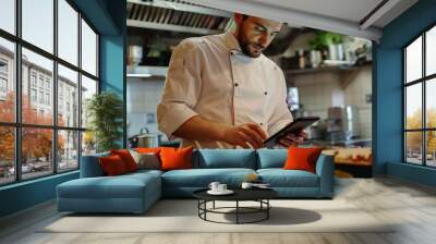 A chef following a recipe on an iPad while cooking in the kitchen, utilizing technology for culinary inspiration and guidance. Wall mural