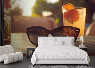 A pair of black sunglasses lying on a sunlit outdoor patio table, with a fresh drink and summer vibe. Wall mural