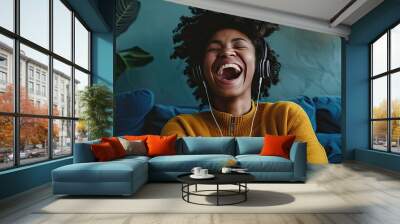 A woman with headphones, sitting on a sofa, laughing out loud while listening to a comedic podcast. Wall mural