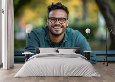 Smiling man with glasses, casual and relaxed, sitting on a park bench Wall mural