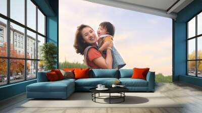 Happy Asian mother plays with daughter and holding girl in hands at park with nice sky, Baby smile and laughing,  Family concept. Wall mural