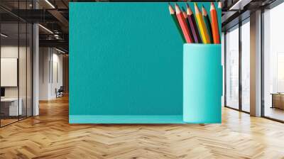 Colorful pencils arranged in a turquoise container against a solid background, perfect for art and creativity themes. Wall mural