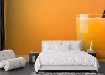 Refreshing orange juice in a glass with a slice and green leaves, set against a vibrant orange background. Wall mural