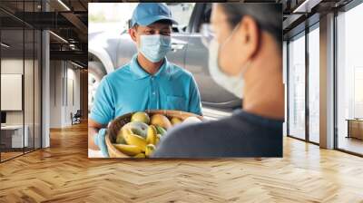 Delivery man volunteer wearing face mask and protective gloves delivering fresh food in bamboo basket from organic farm to senior people home in Coronavirus (COVID-19) pandemic. Wall mural