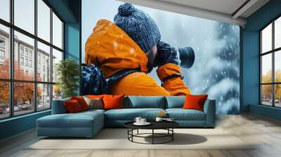 Photographer in orange jacket taking pictures in snowy landscape, capturing winter beauty and adventure with a camera in cold weather conditions. Wall mural