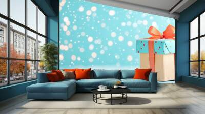 A beautifully wrapped gift box sitting on a light blue surface with snowflakes in the background Wall mural