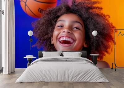 A joyful child with curly hair catches a basketball on a colorful background during a daytime game Wall mural