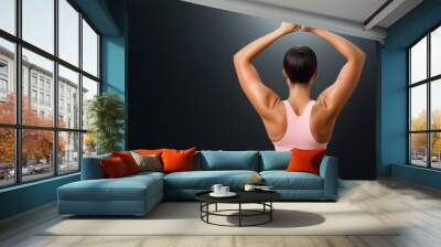 A woman shows off her strong arms while posing against a dark background in a fitness setting Wall mural