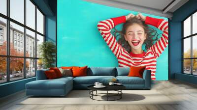 Girl with curly hair smiles joyfully against a teal background Wall mural