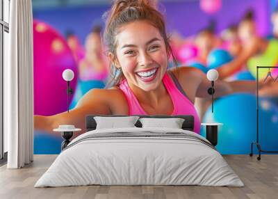 Joyful young woman exercising with colorful fitness balls in a vibrant gym during a group class Wall mural