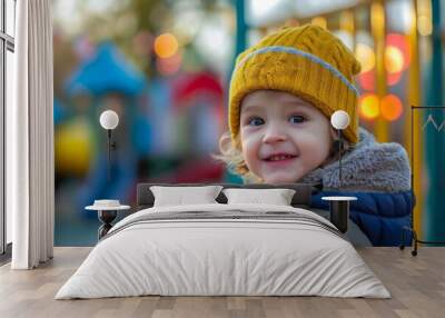 A joyful toddler sporting a sunny yellow hat and jacket plays with a smile on their face at the playground Wall mural