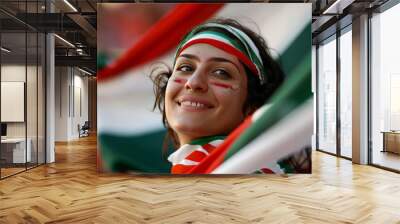 A youthful woman looks upwards with a hopeful expression, draped in her national flag at a sports event Wall mural