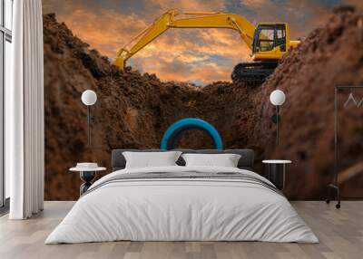 Crawler excavator is digging in the construction site pipeline work on sunset sky background Wall mural