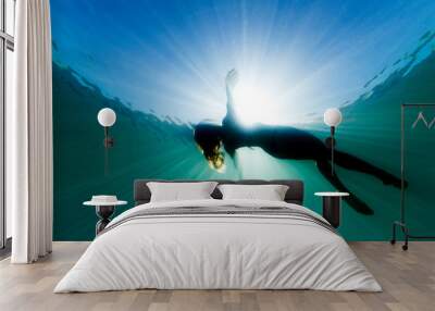 A beautiful woman floats on her back in the ocean as she is surrounded be bright ethereal light and sun rays. Wall mural