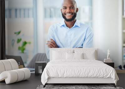 Confident business man standing with arms crossed in an office, looking proud and happy alone at work. Portrait of a smiling, cheerful and professional African male boss working in corporate Wall mural