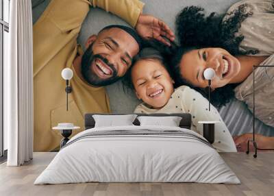 Happy family, above and kid smile or happy with parents together in the morning laughing in a bedroom on a bed. Relax, mom and dad enjoy quality time with kid with happiness, bonding and love Wall mural