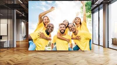 Multiracial smiling friends dressed in yellow doing the piggy back - Lifestyle concept of volunteers doing great teamwork - Group of happy young people having fun together Wall mural