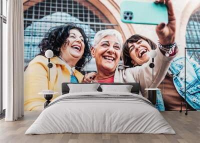 Three cheerful women chilling outside taking group selfie and smiling - Happy female senior friends enjoying the weekend together while sightseeing an italian city - Elderly people lifestyle concept. Wall mural