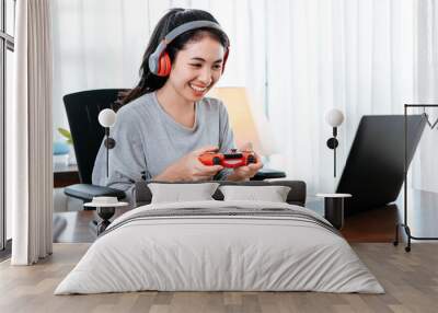 Funny Young woman wearing earphones playing computer game on laptop with joypad. Wall mural