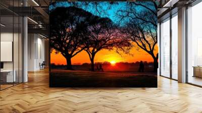 A beautiful sunset over a park with a few people sitting on chairs Wall mural