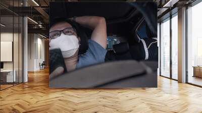 bored car driver waiting in a traffic jam, Young asian man wear a mask while using a mobile phone while driving in city. Wall mural