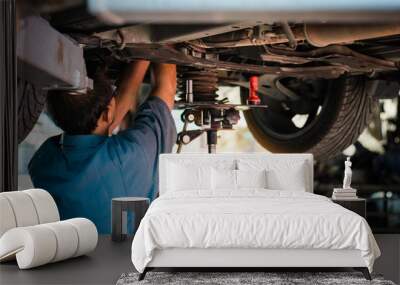 Mechanic repairing a car, Mechanic inspects car suspension system and chassis with a torch-lite under the car. Wall mural