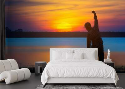 Silhouette of a young man with outstretched arms at sunset on a lake,Winner on a Dam. Active life concept. Wall mural