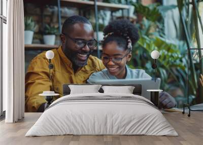 A father helping his cheerful teenage daughter with homework at home, both smiling and working together on a laptop Wall mural