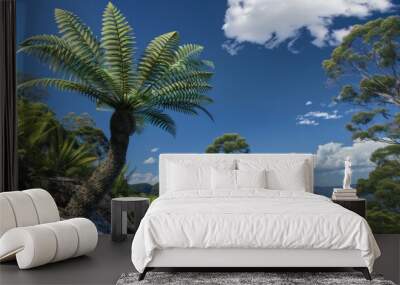 A lush fern tree grows on a cliff overlooking a valley with a blue sky and fluffy clouds. Wall mural