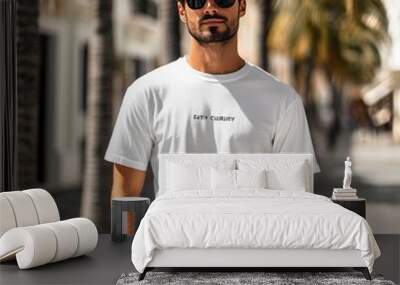 A man in a white t-shirt stands confidently on a sunny street lined with palm trees. Wall mural