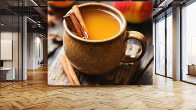 A mug of apple cider with cinnamon sticks, an apple and a wooden background. Wall mural