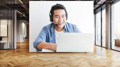 Asian handsome man in blue shirt using laptop with headphone talking smile and happy face Wall mural