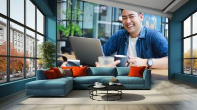 Asian man in blue shirt talking and smile with friend in coffee shop cafe Wall mural