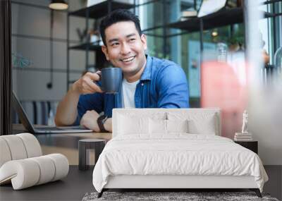 Young Asian Man in blue shirt working with laptop in coffee shop cafe smile and happy face Wall mural