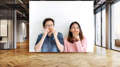 Attractive asian hungry couple eating pizza or fast food with smile and tasty facial expression on face with white wall background. Millennial lifestyle with friends concept. Man and woman enjoy meal. Wall mural